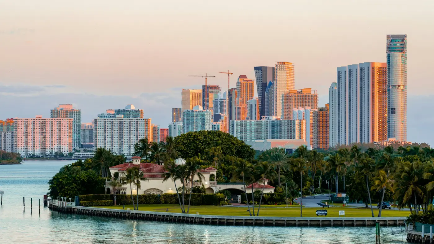 Miami towers at sunset behind palm trees and a waterfront home