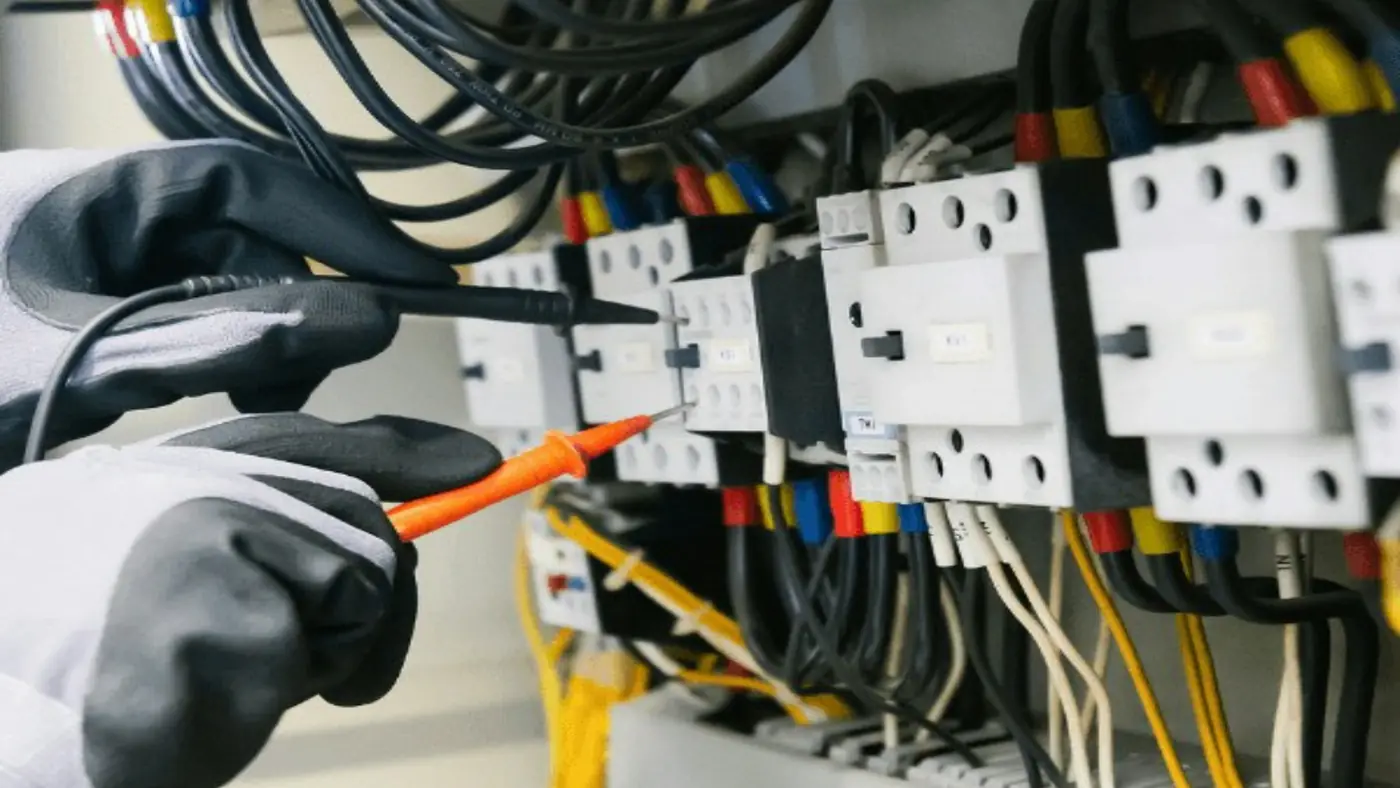 Mãos com luvas testando com um medidor a fiação de um quadro elétrico