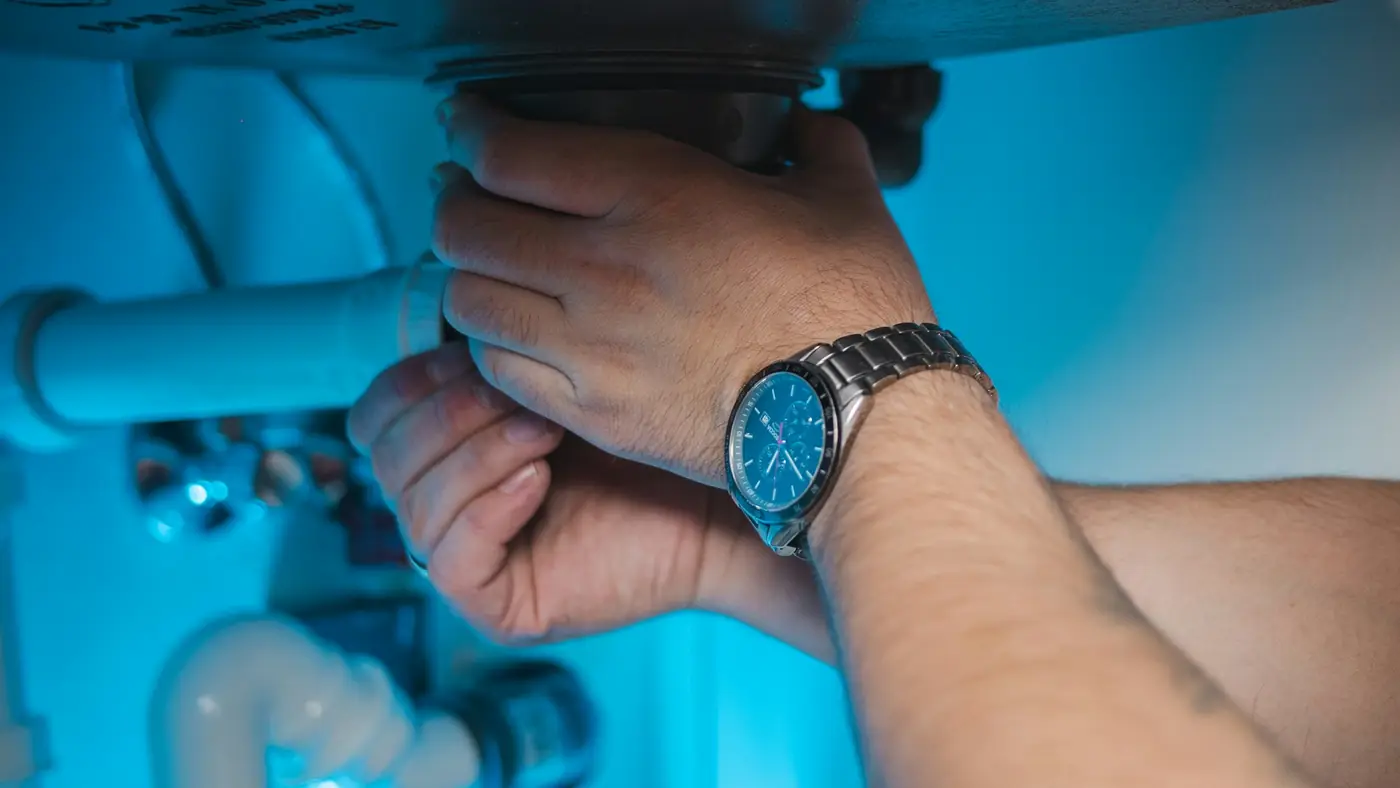 A plumber’s hands tightening a pipe under a sink
